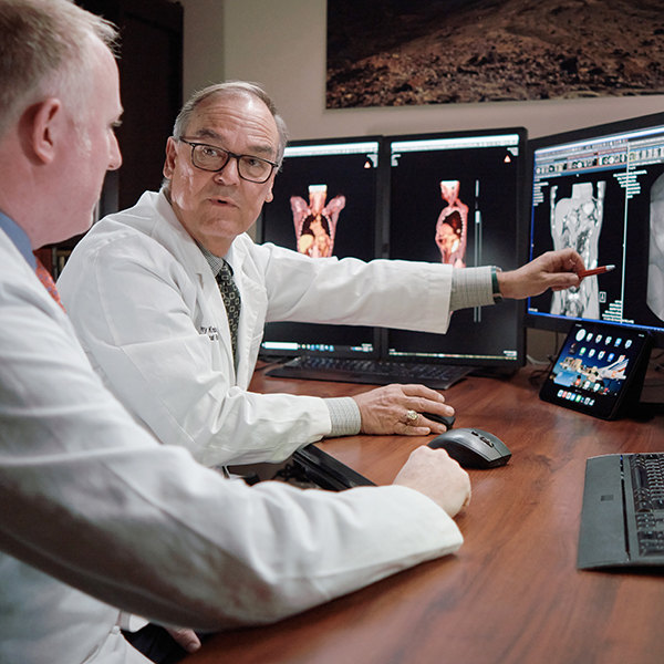 A female and male doctor discuss imaging results while treating a patient with throat cancer.
