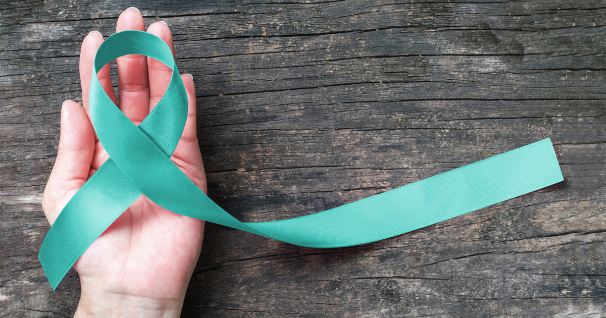 A hand holding the teal blue cervical cancer support ribbon