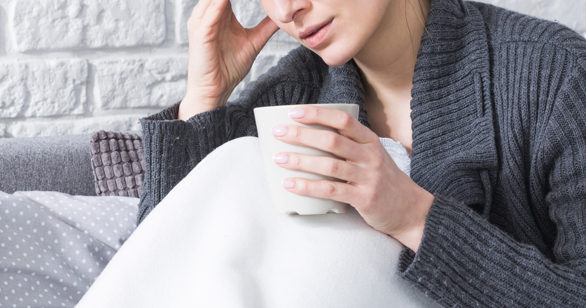 A woman with the flu covered with a blanket and drinking hot tea