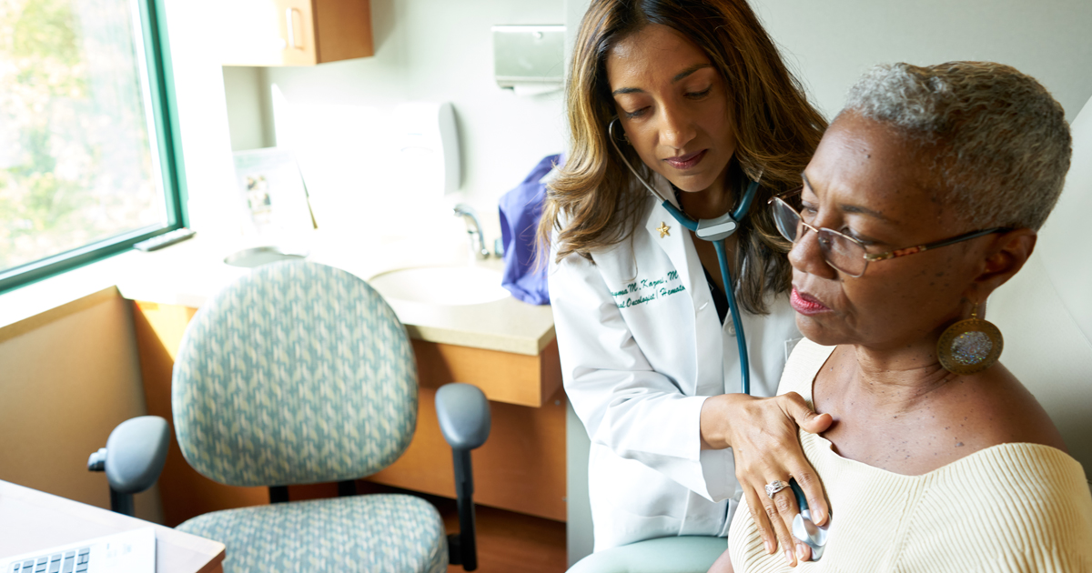 A female oncologist using a stethoscope to listen to a cancer patient's breathing