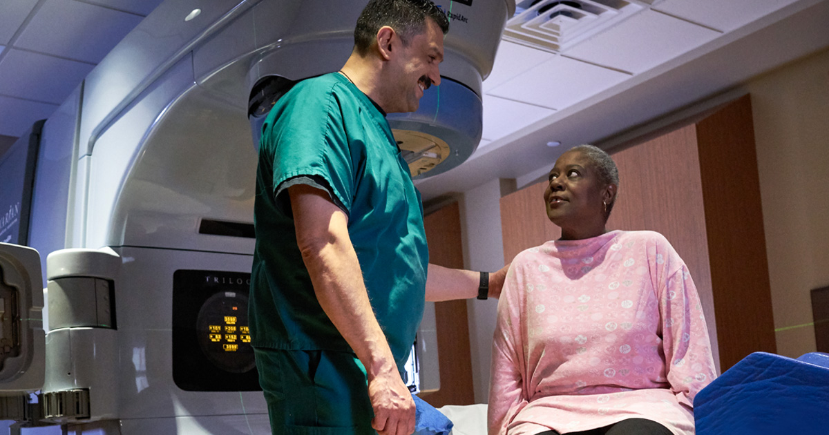 A male doctor in scrubs assisting a female patient undergoing radiation